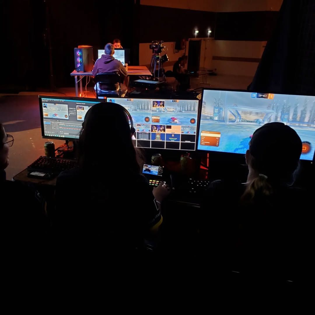 Deux silhouettes de deux jeunes filles devant 3 écrans, de gauche à droite : l'interface de OBS Studio, le multiview avec des caméras, des captures du jeu Rocket League, des visuels... Et un écran avec le jeu en plein écran. Devant les écrans, des claviers d'ordinateur et des 